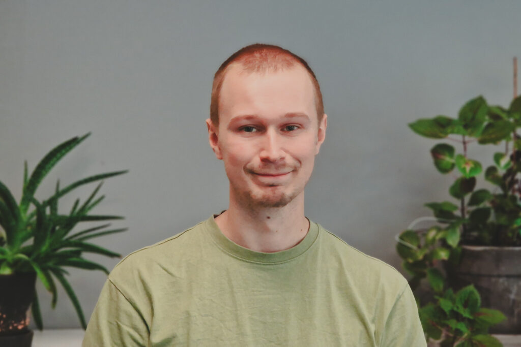 Porträttfoto av Axel Gunnemyr i en collegetröja och med växter i bakgrunden.